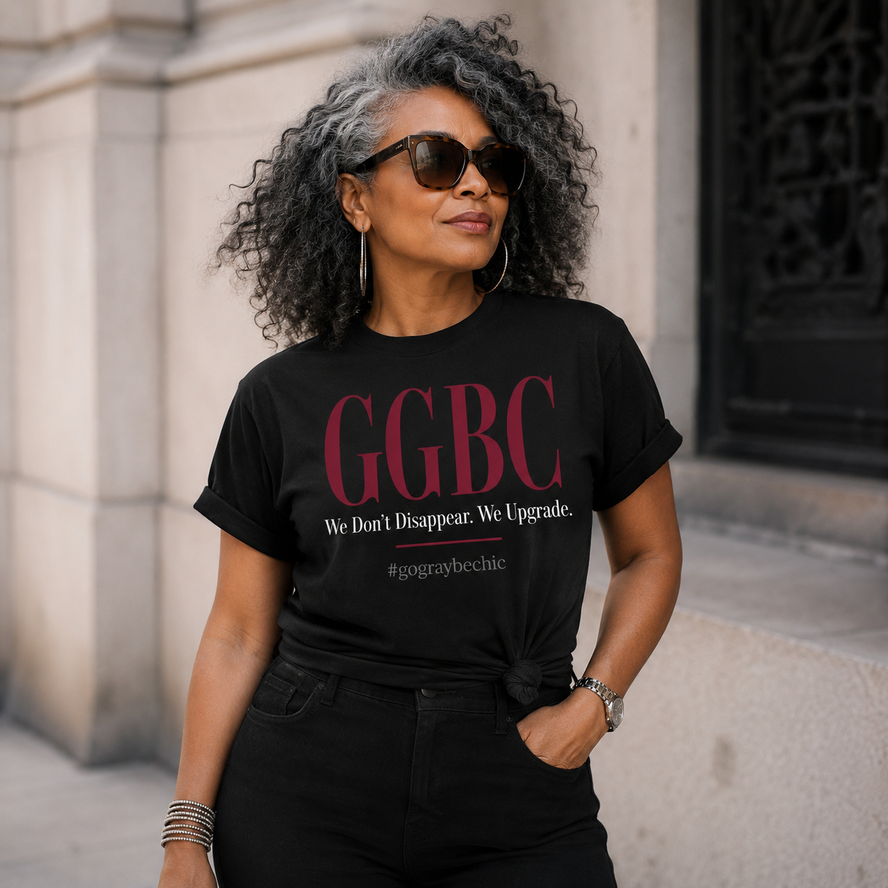 Woman wearing a black t-shirt with 'GGBC' text, standing against an urban background.