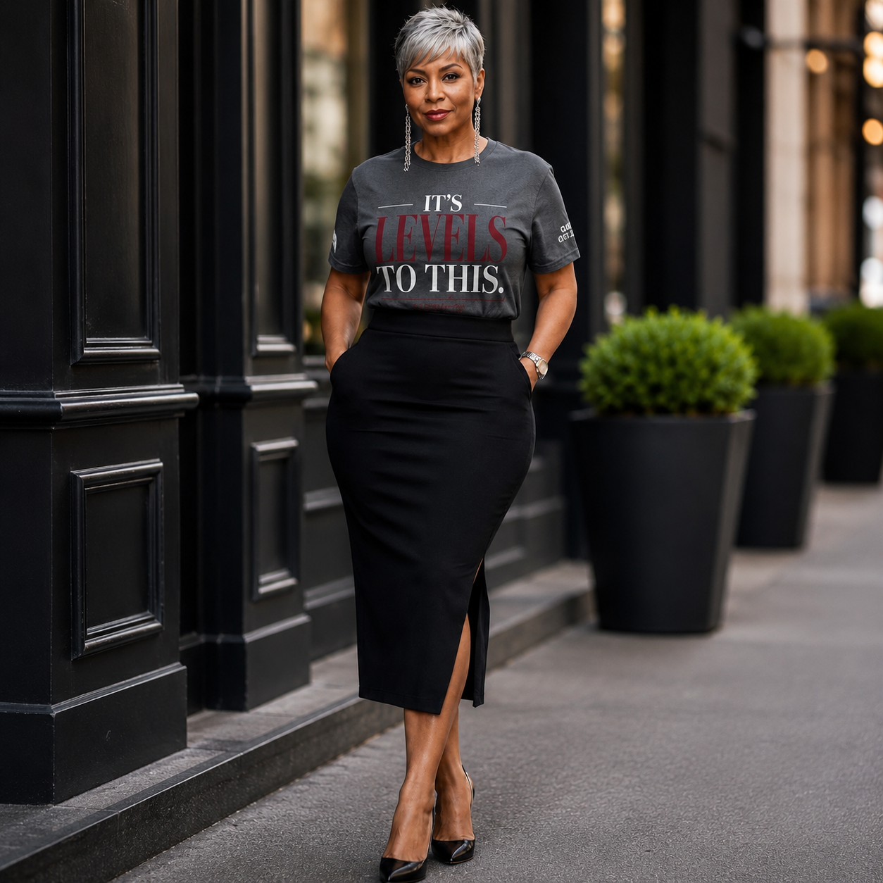 Woman wearing a gray t-shirt with text and a black skirt standing on a city street.